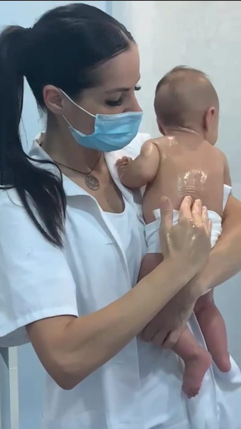 Encarni, con mascarilla, masajea con suavidad la espalda de un bebé que sostiene en brazos